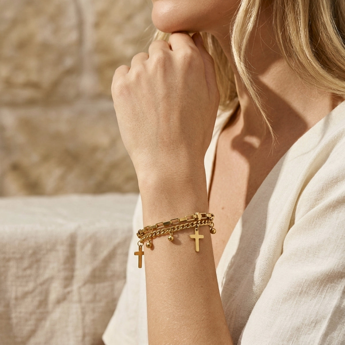 Side lifestyle view of a model wearing the gold-tone layered cross and bead charm bracelet with a white linen dress.