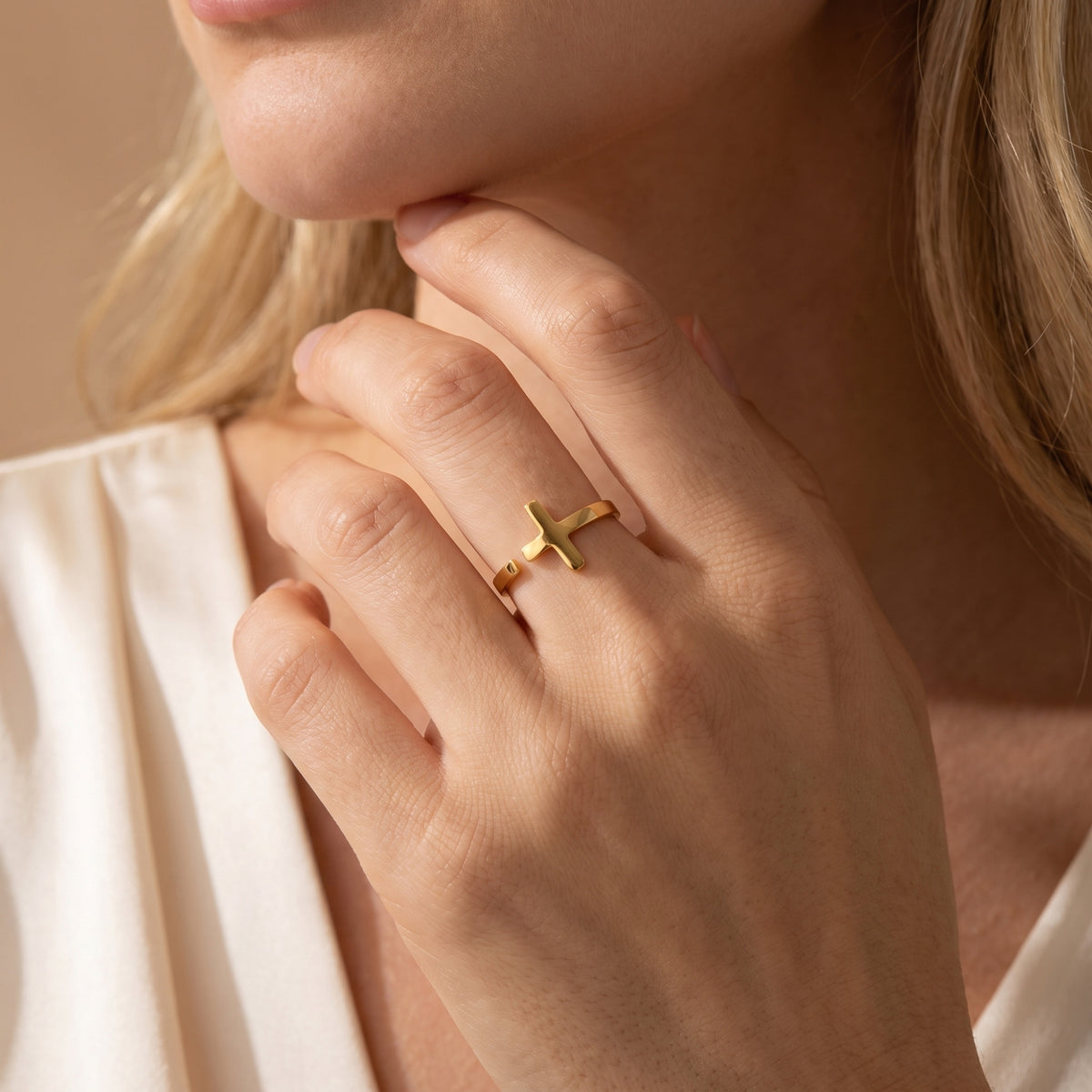 Close-up of the gold-tone cross open ring on a model's middle finger near her chin.
