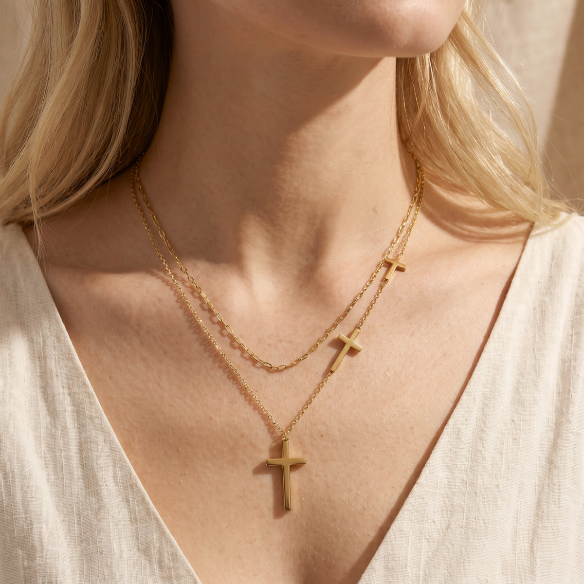 Front close-up of the gold-tone layered cross necklace worn over a white textured V-neck top.