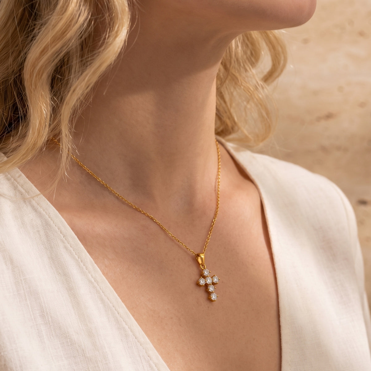 Side view of a model wearing the gold-tone cubic zirconia cross necklace with a white garment