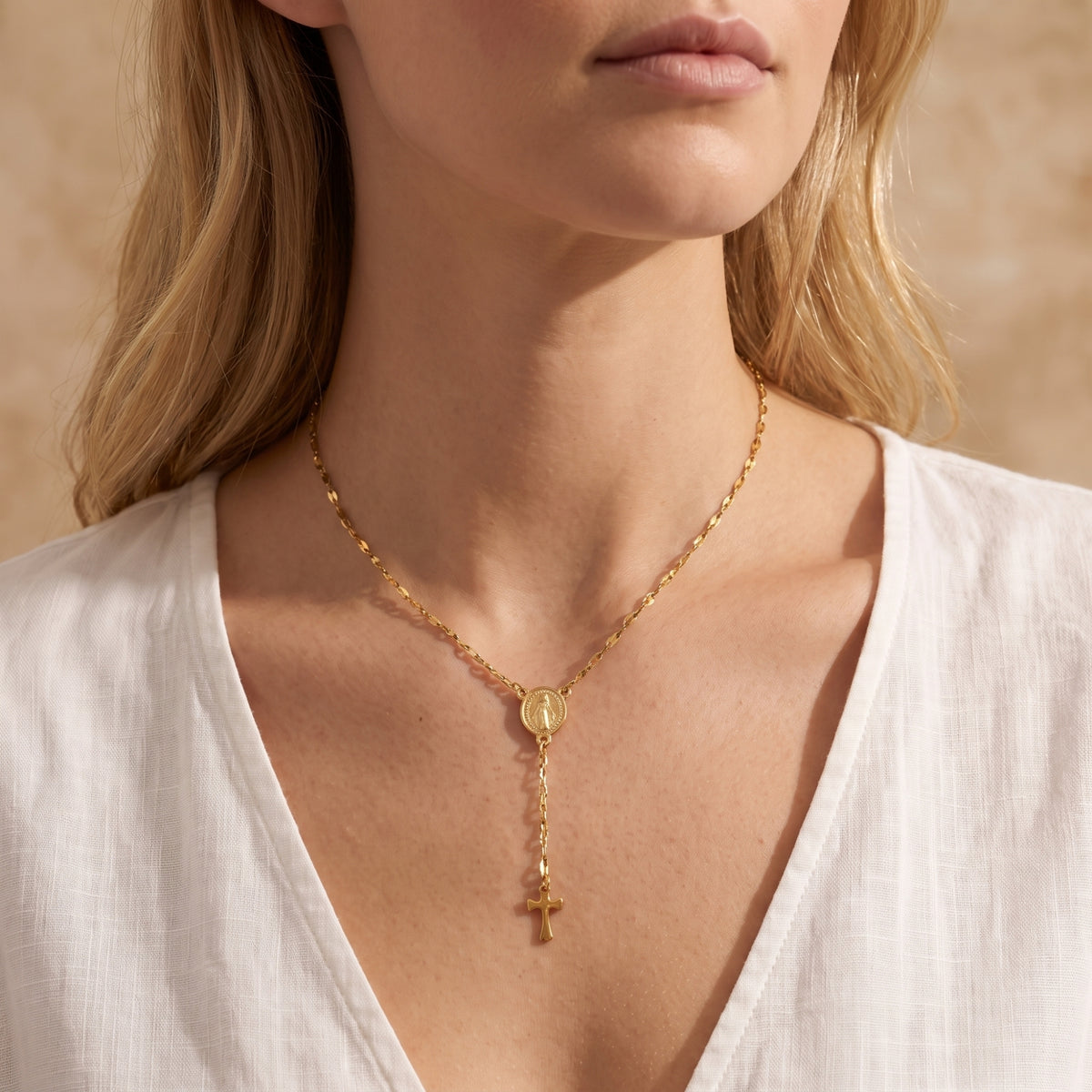 Frontal view of a model wearing the gold-tone rosary station cross necklace against a V-neck white top.