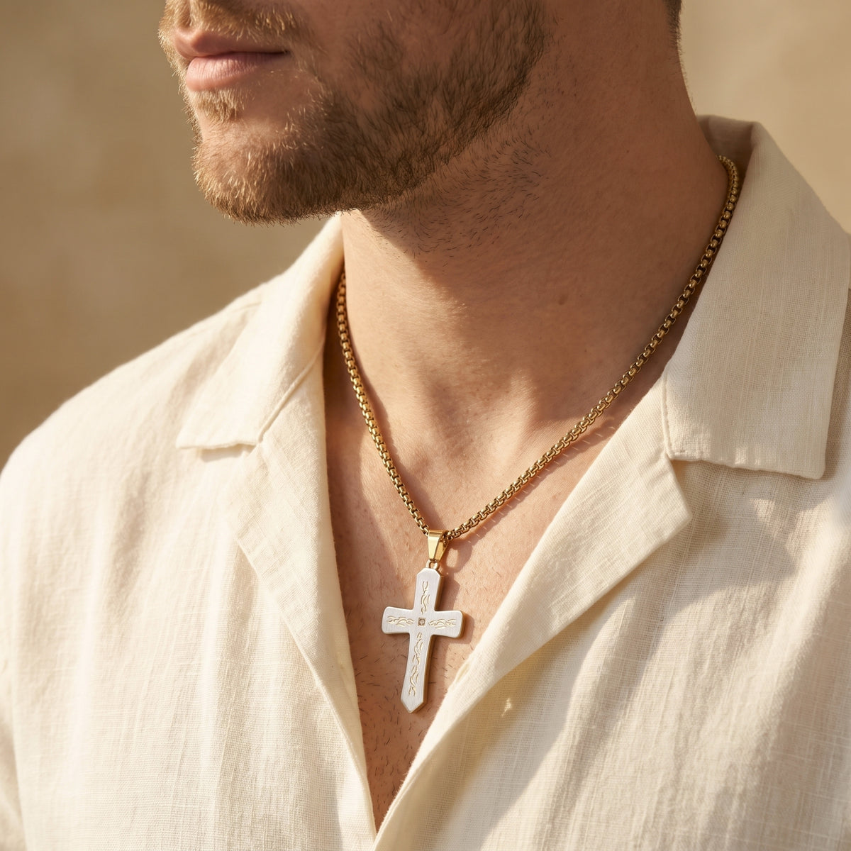 Three-quarter view of a man wearing a two-tone cross necklace with a gold-tone box chain over a white shirt.