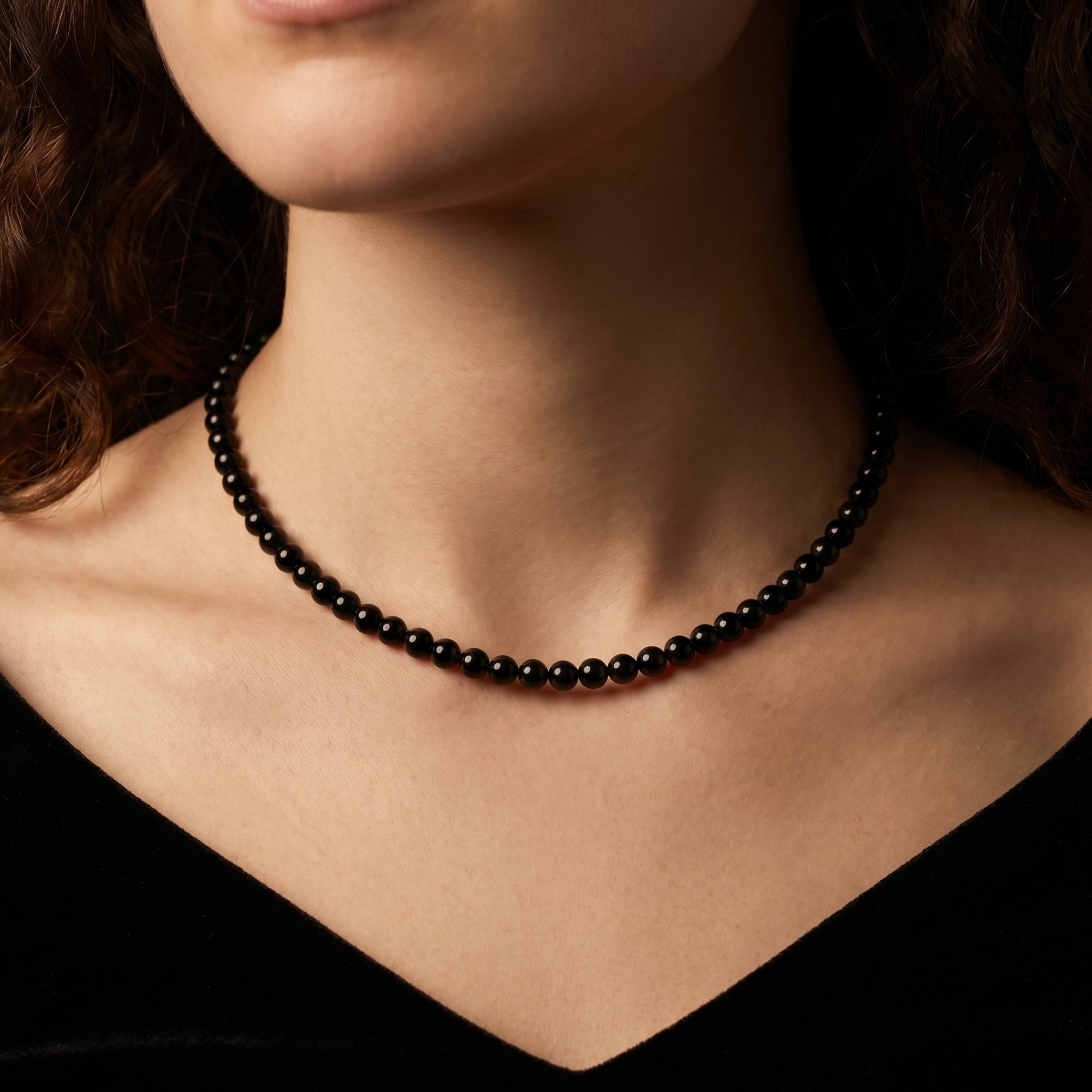 Frontal view of a model wearing the 6mm round black onyx beaded necklace with a black velvet garment.