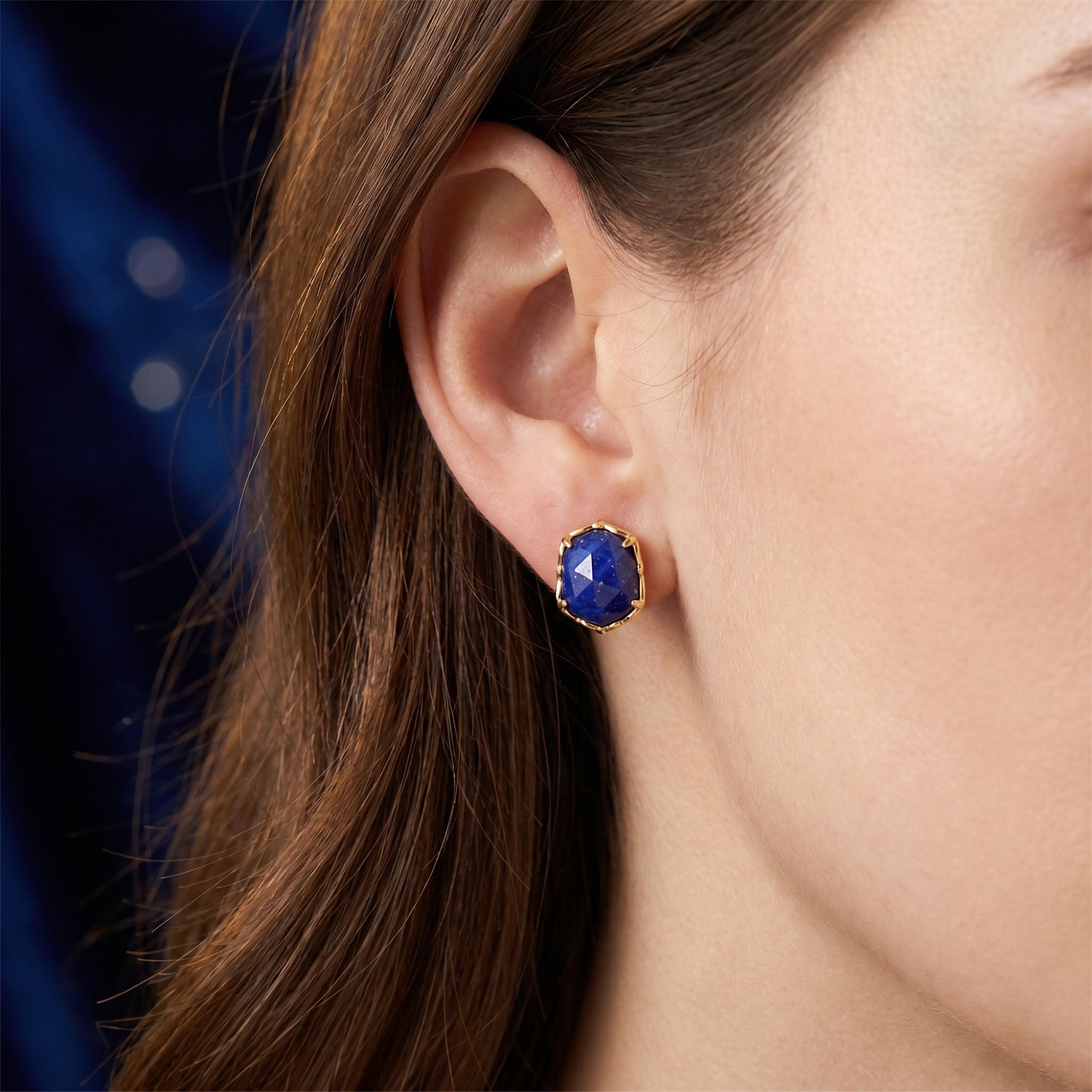 Side view of a gold hexagon stud earring with a natural blue lapis lazuli stone worn on a model's ear.