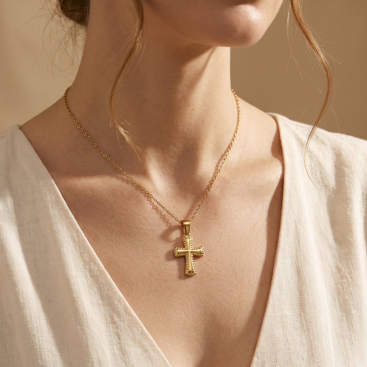 Gold-tone beaded cross necklace worn over a cream V-neck top.
