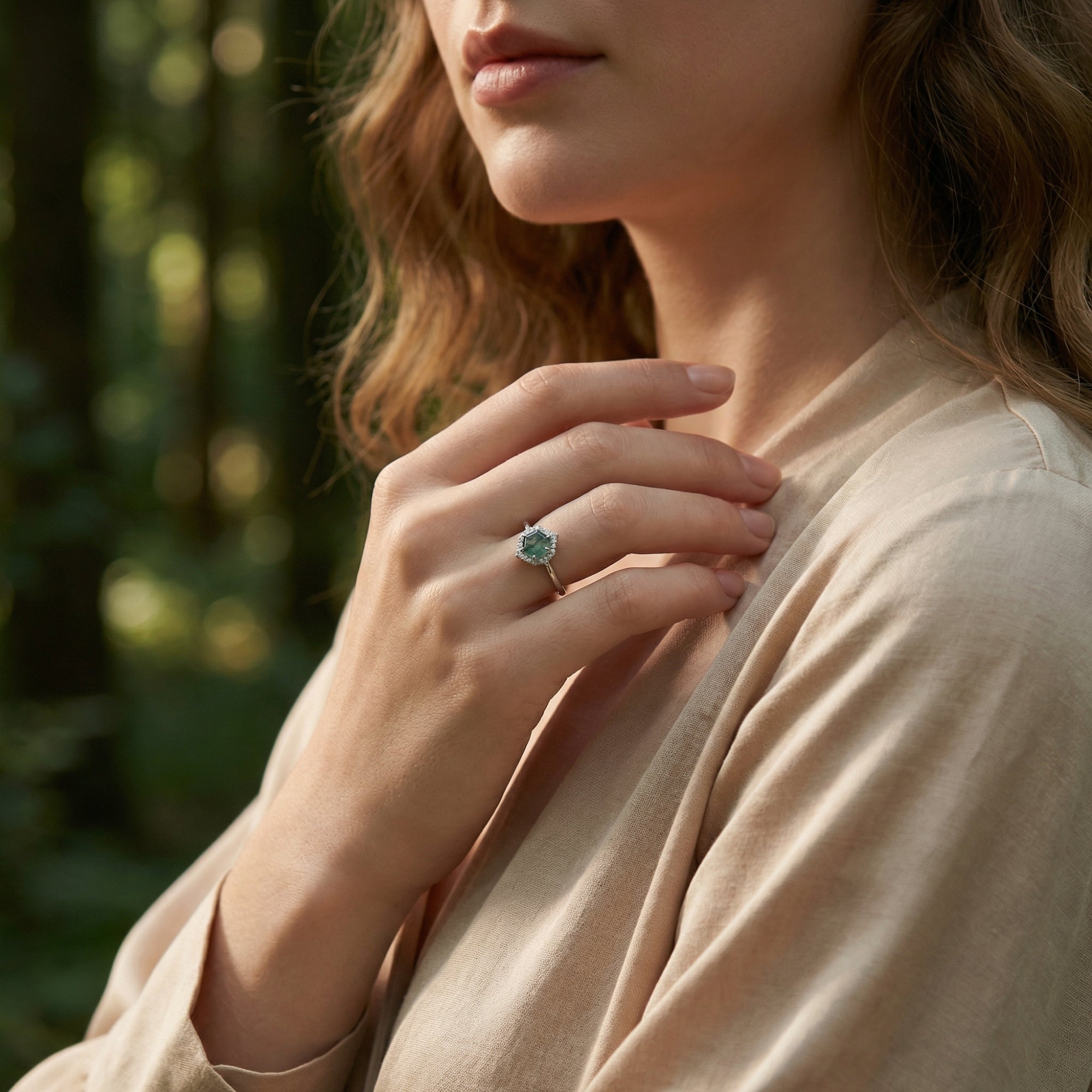 Sterling silver hexagonal moss agate halo ring worn by a model against a soft forest background.