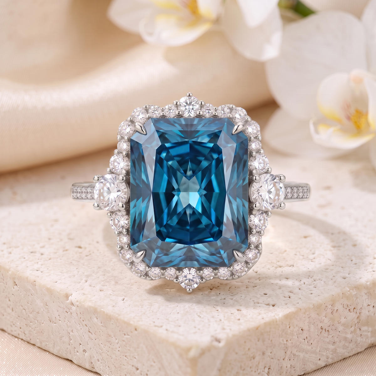 Frontal view of a radiant cut blue moissanite halo ring in white gold displayed on a stone platform.
