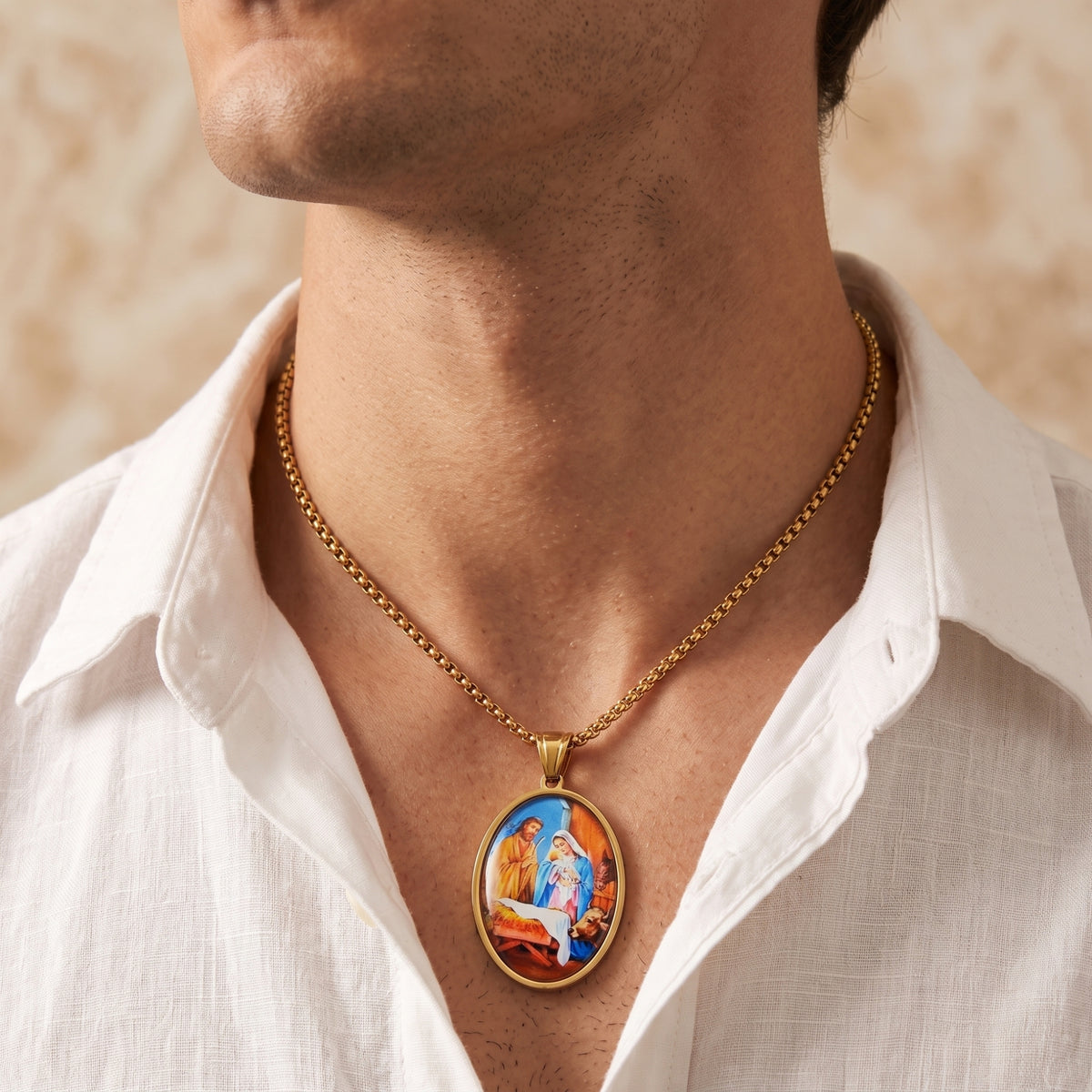 Gold-tone oval Nativity pendant necklace worn at the chest by a man in an open-collar white shirt.