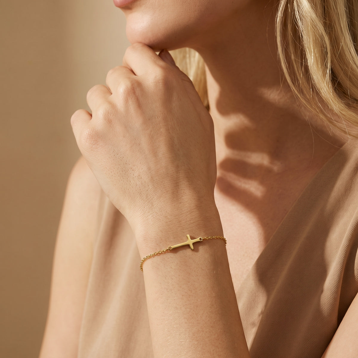 Close-up of a gold-tone horizontal cross bracelet worn on a woman's wrist near her chin.