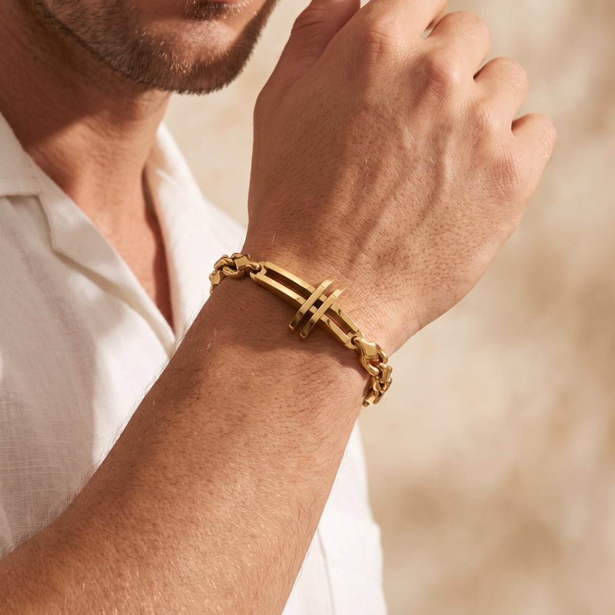 Close-up of a man wearing the gold-tone cross link bracelet on a raised wrist beside a white shirt.
