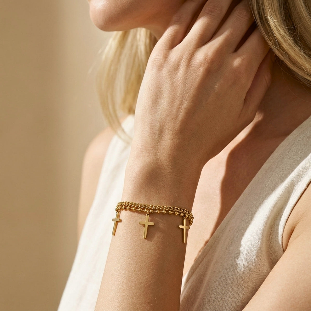 Person wearing the gold double-strand cross charm bracelet with three dangling crosses, shown beside the neck and shoulder.