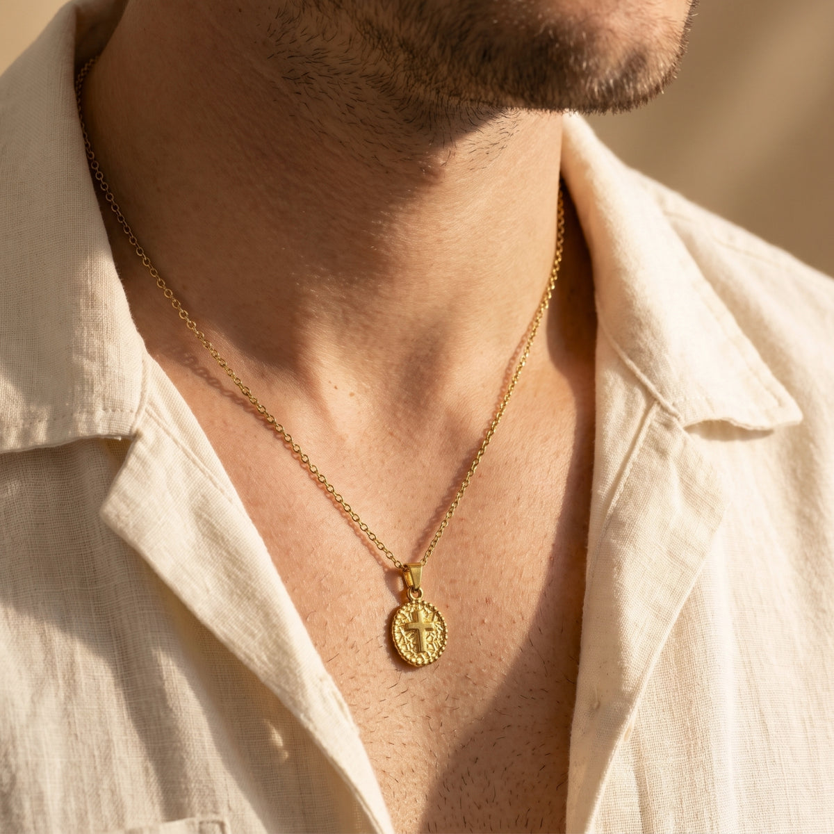 Gold-tone cross medallion necklace worn on a man's chest with an open-collar white shirt
