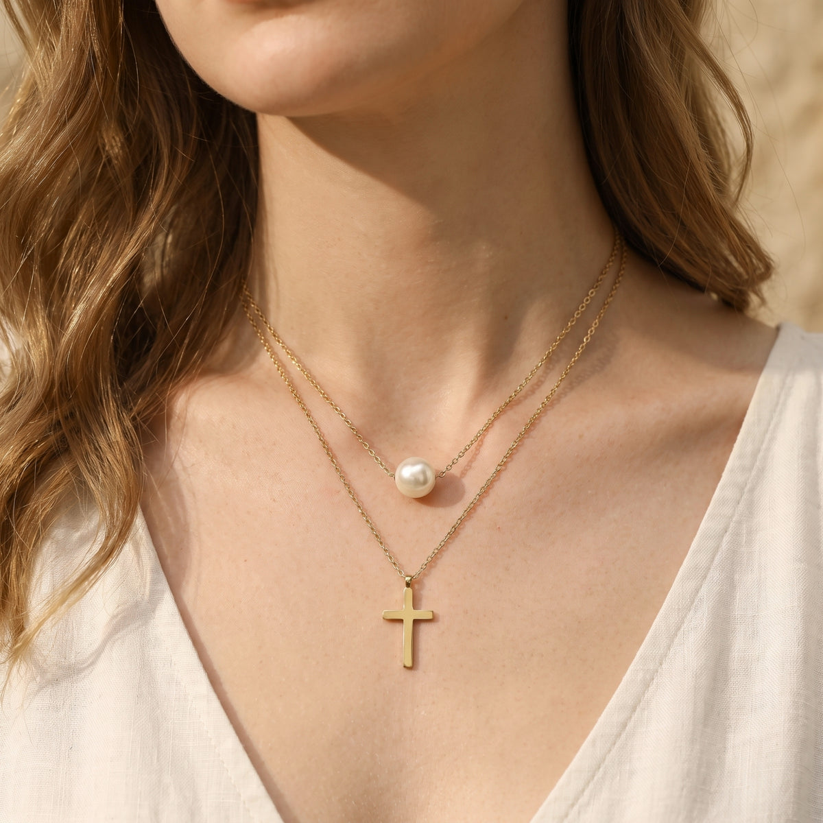 Front-facing close-up of a model wearing the layered gold-tone necklace with a pearl station and cross pendant.