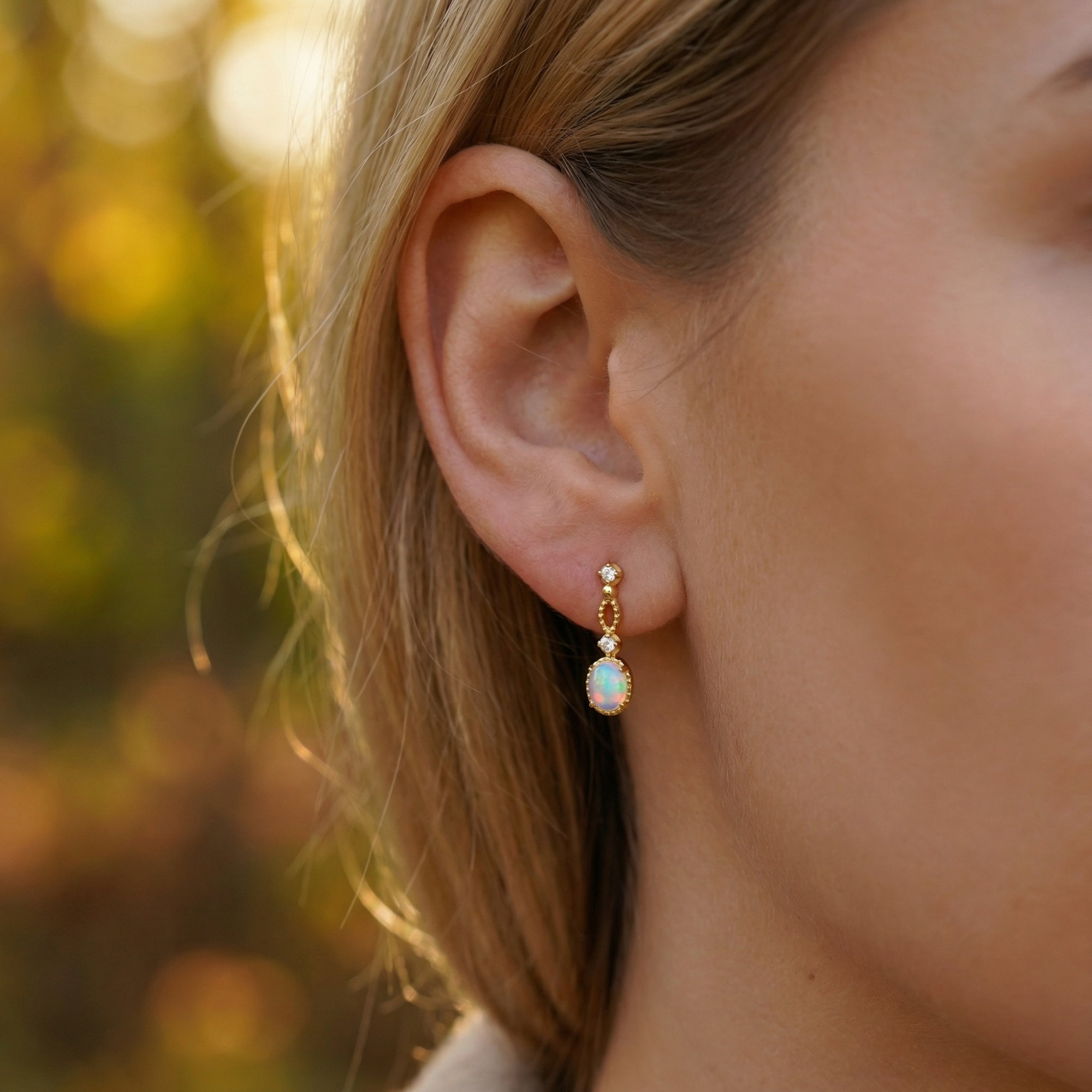 Profile view of a model wearing the dainty gold-tone Lorelei oval white opal drop earrings in natural light.