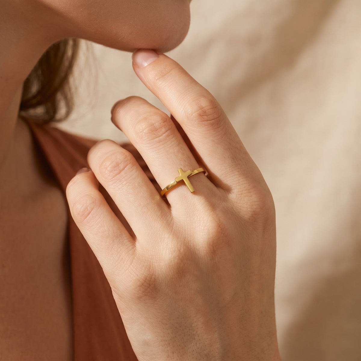 Side perspective of a model wearing the gold-tone cross ring with hand raised near her face.