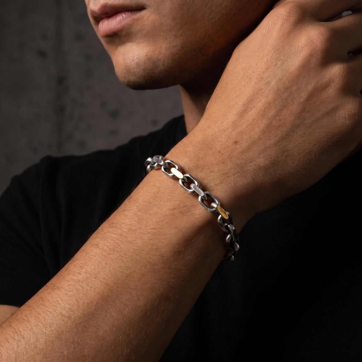 Side view of a man wearing the heavy silver link bracelet with gold-tone accents and a black shirt.