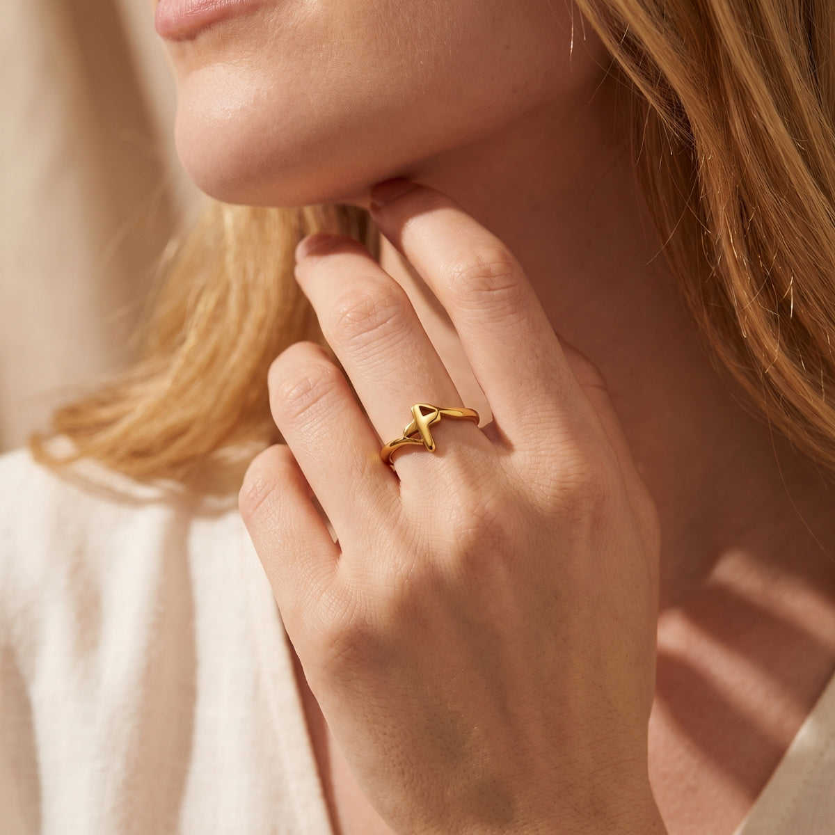Close-up of a woman wearing the gold-tone openwork cross ring with her hand beneath her chin.