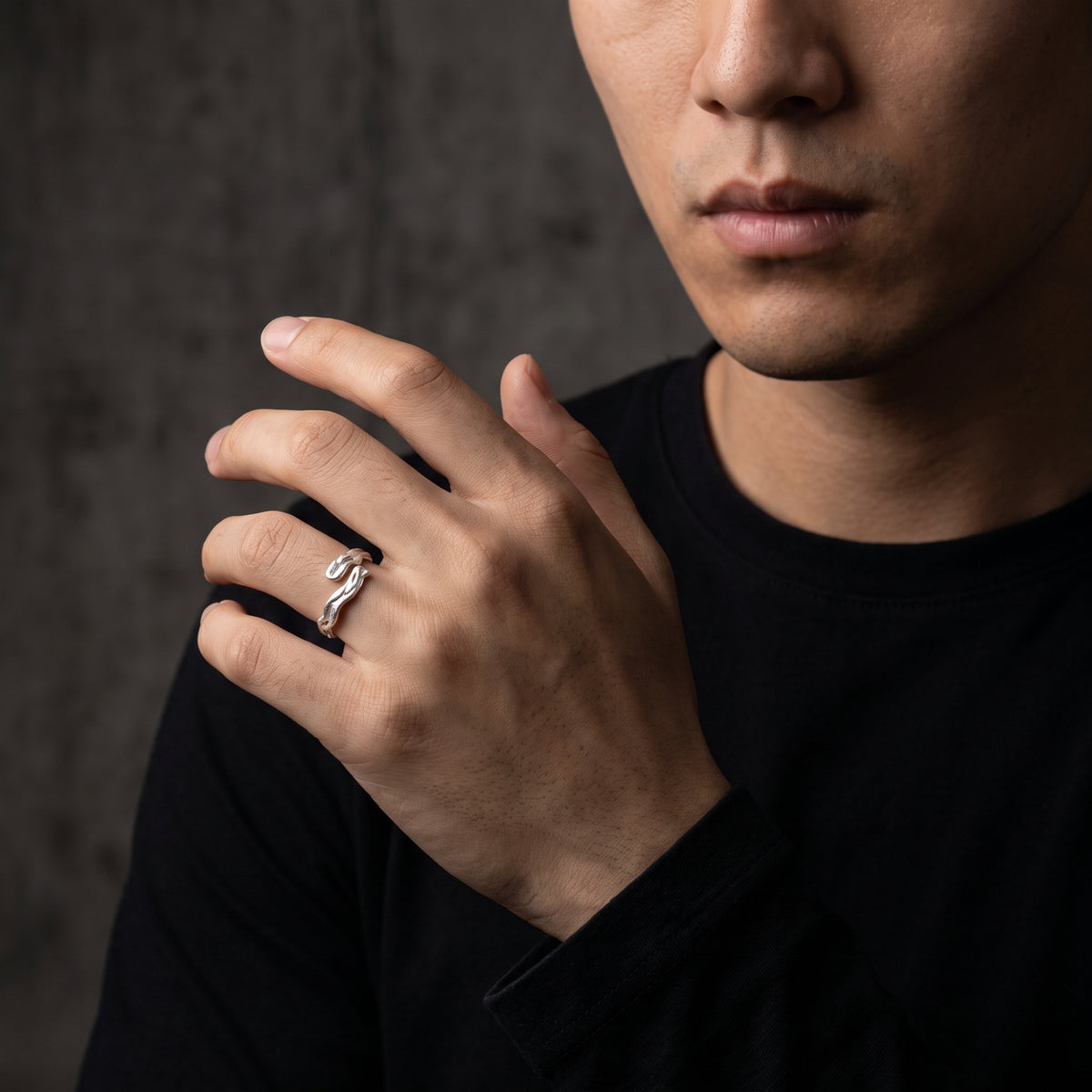 Male model displaying the textured silver open ring on his ring finger near his chest.