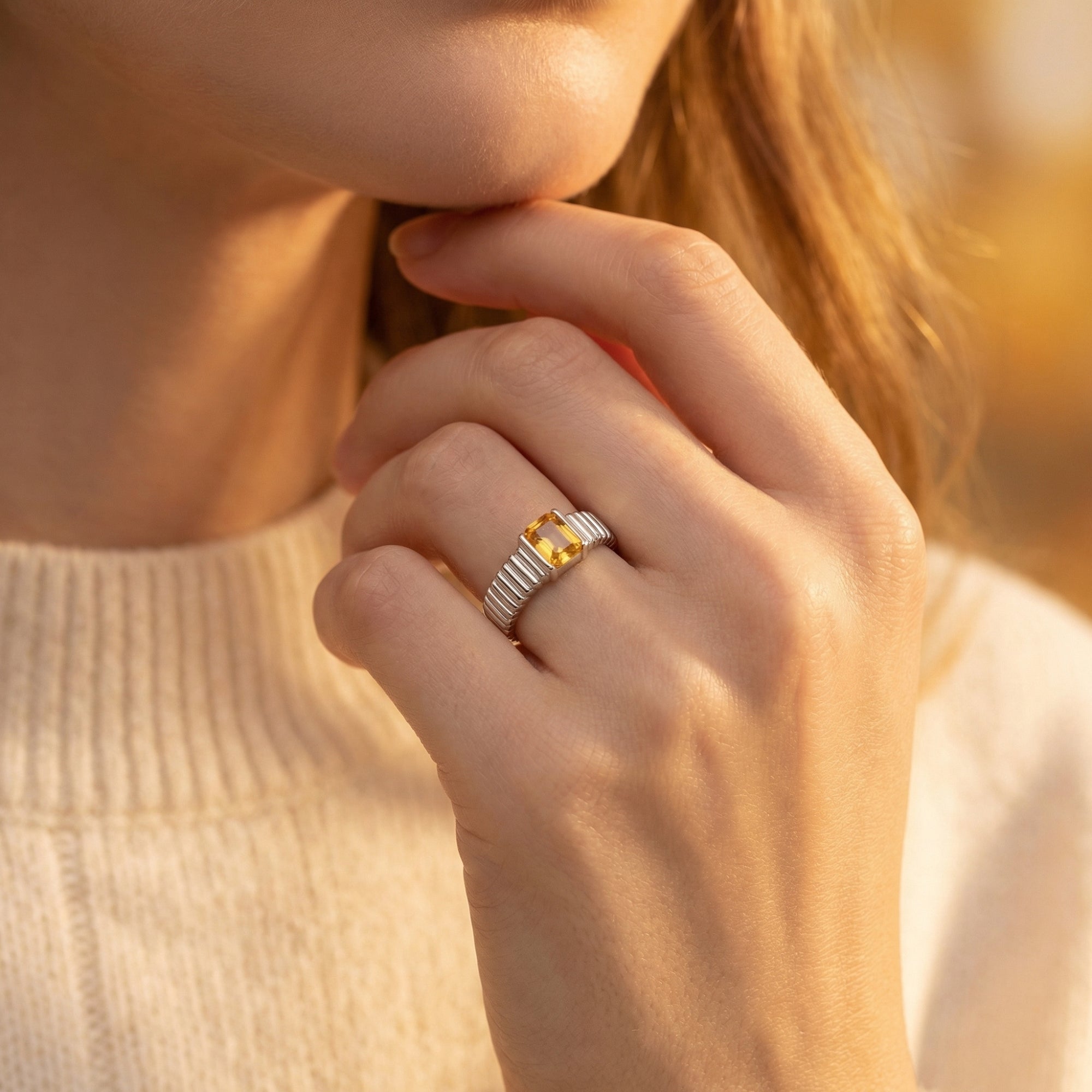 Natural citrine silver ring with an emerald-cut stone worn on a model's finger in soft light.