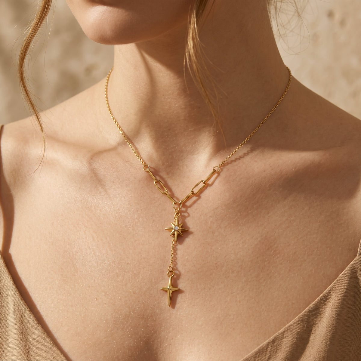 Frontal close-up of a model wearing the gold-tone lariat necklace with a stone-set starburst and dangling cross-shaped drop.