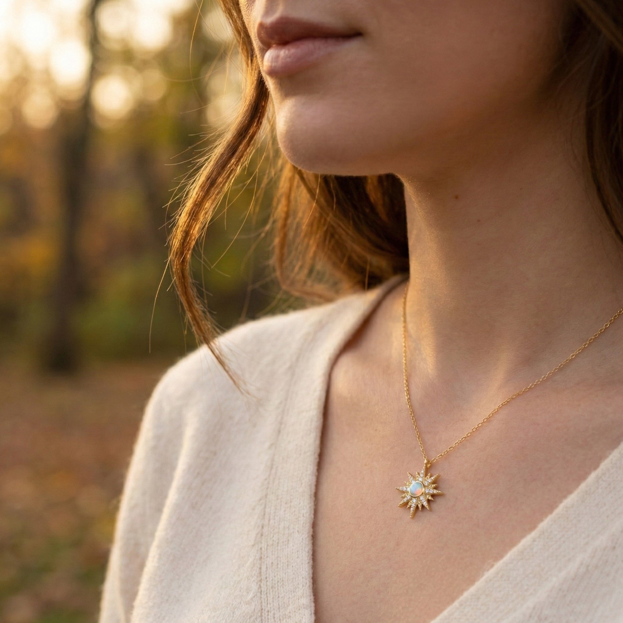 Lifestyle view of a model wearing the gold starburst opal pendant necklace against a blurred autumn background.