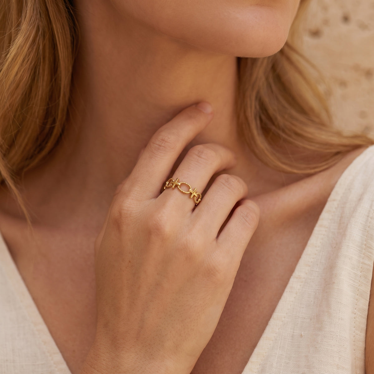 Close-up of a gold-tone open cross ring worn on a model’s ring finger near her neck.