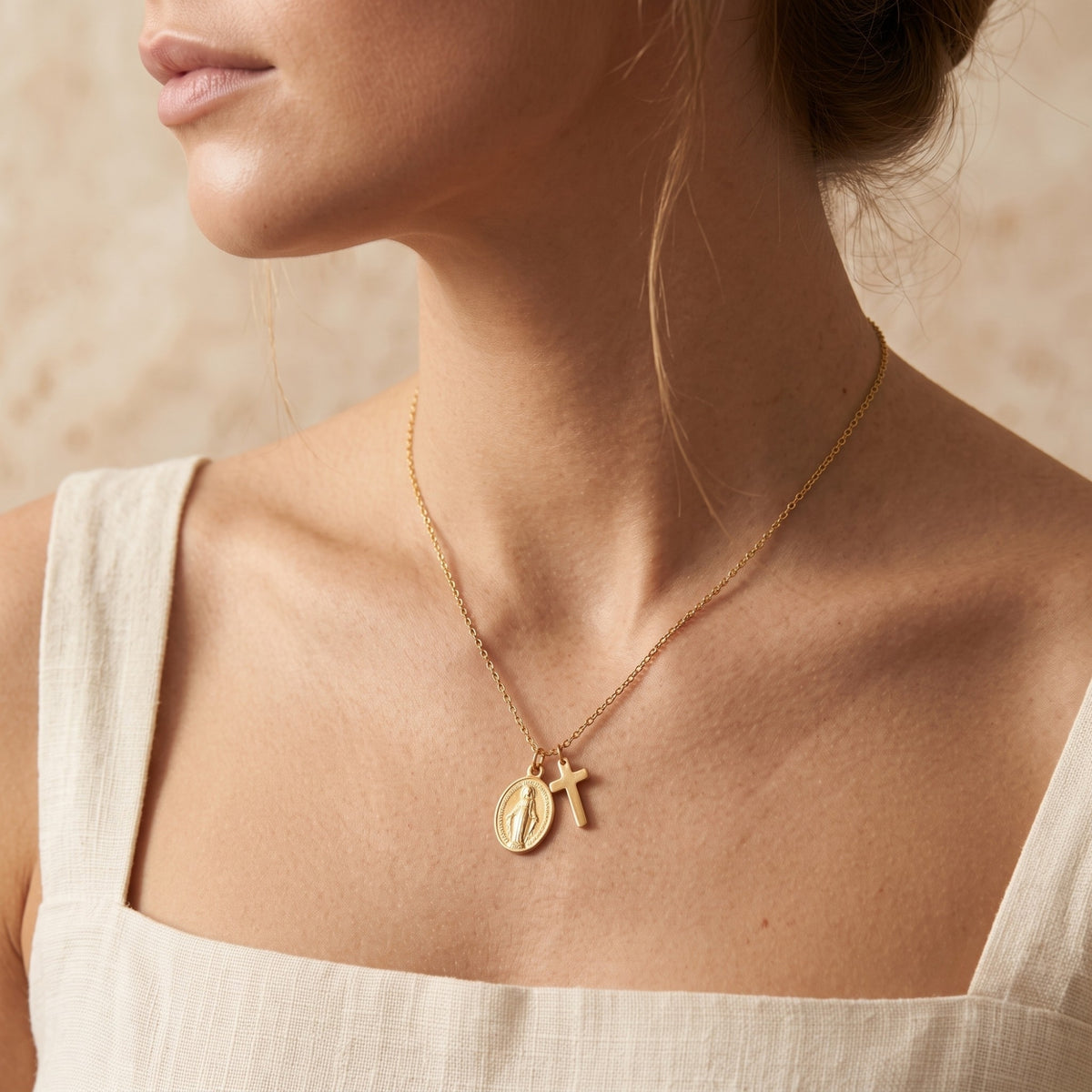 Model wearing the gold-tone cross and oval medal necklace over a white top.
