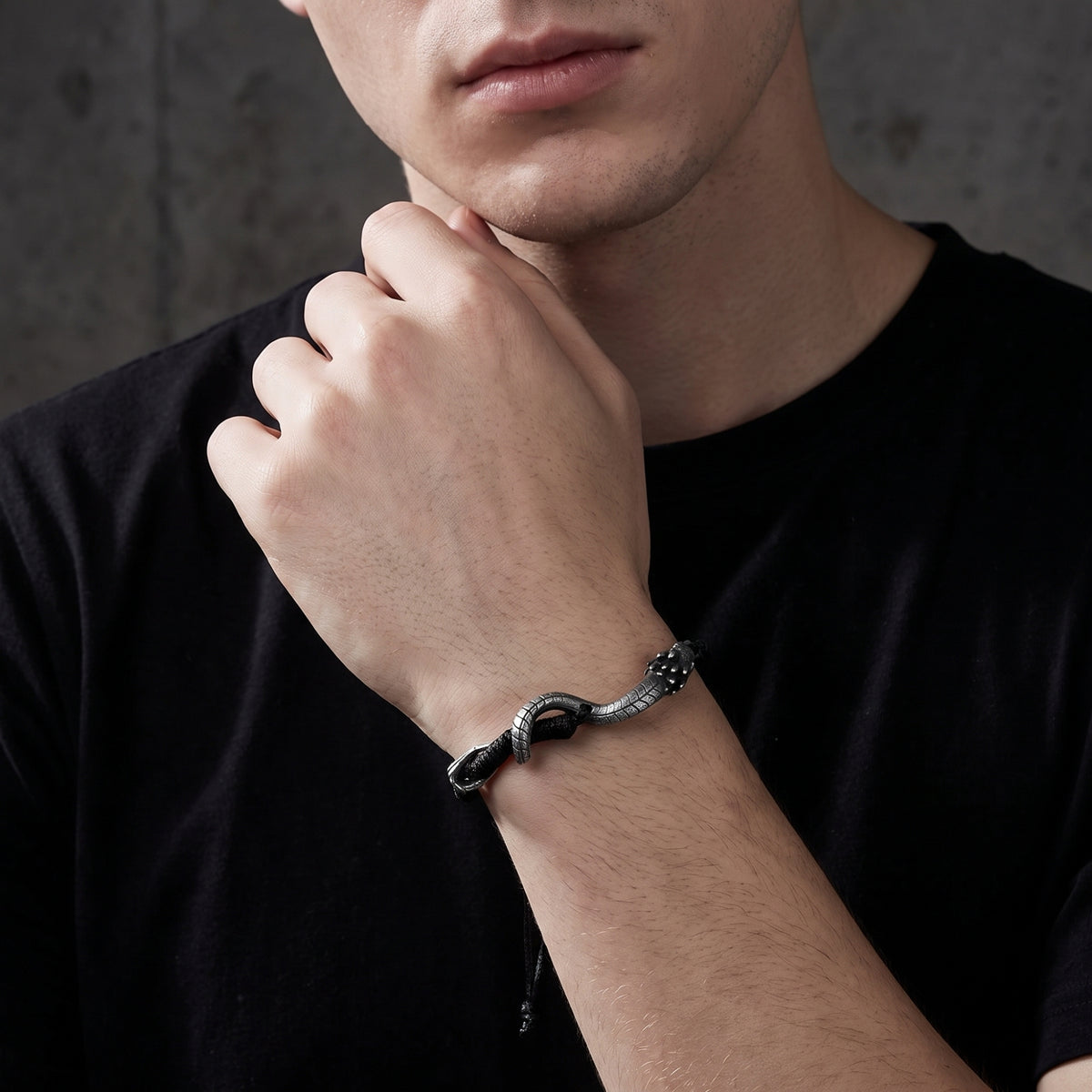 Close-up of a man wearing the black cord serpent bracelet, with his raised wrist near his chin.