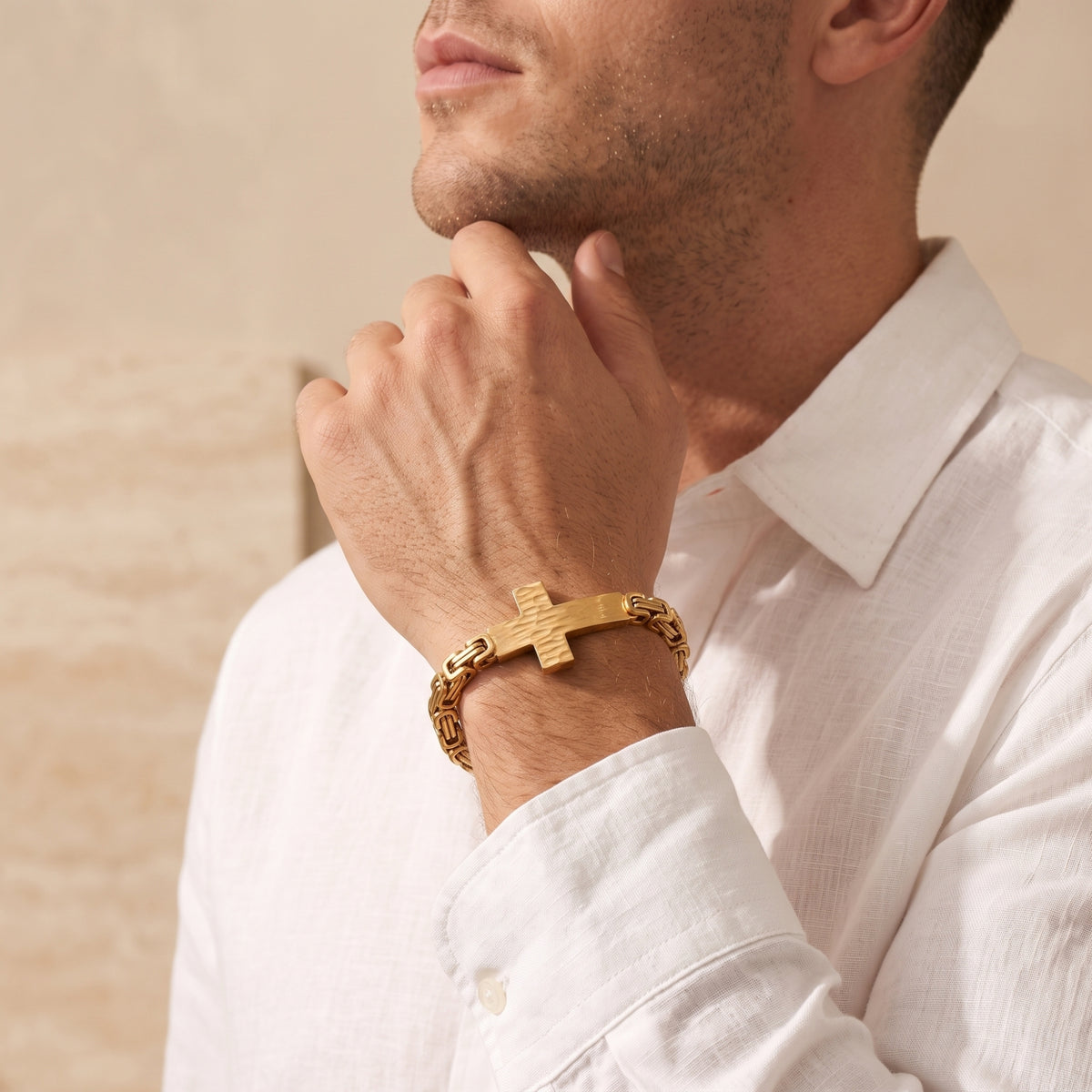 Model wearing a white shirt and the gold-tone hammered cross bracelet, resting his hand near his chin.