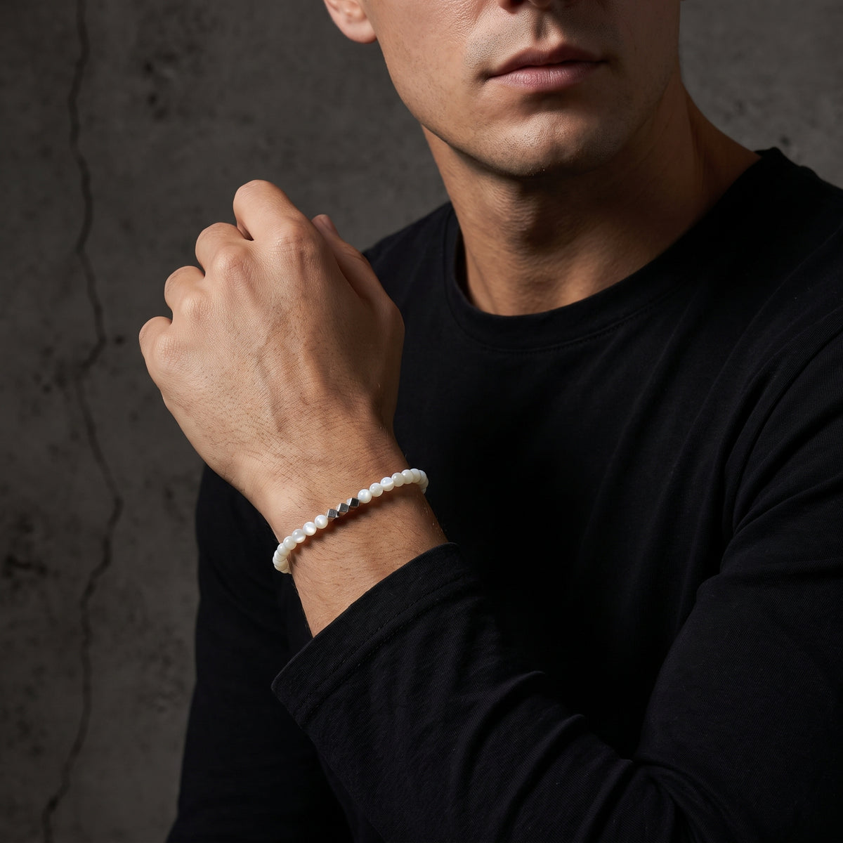 Cropped view of a man wearing the white beaded bracelet with silver cube accents over a black crew-neck shirt.
