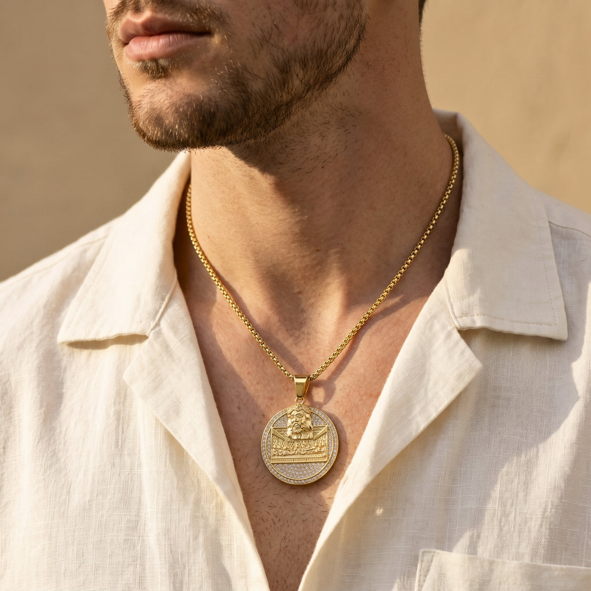 Man wearing the gold-tone Last Supper medallion necklace over an open cream shirt, shown in a wider chest-level crop.