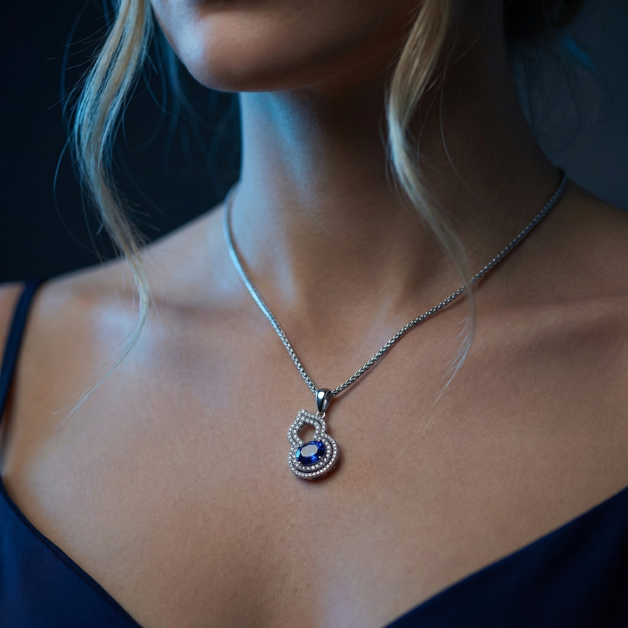Side view of a woman wearing a white gold natural tanzanite halo necklace with a gourd-shaped pendant.