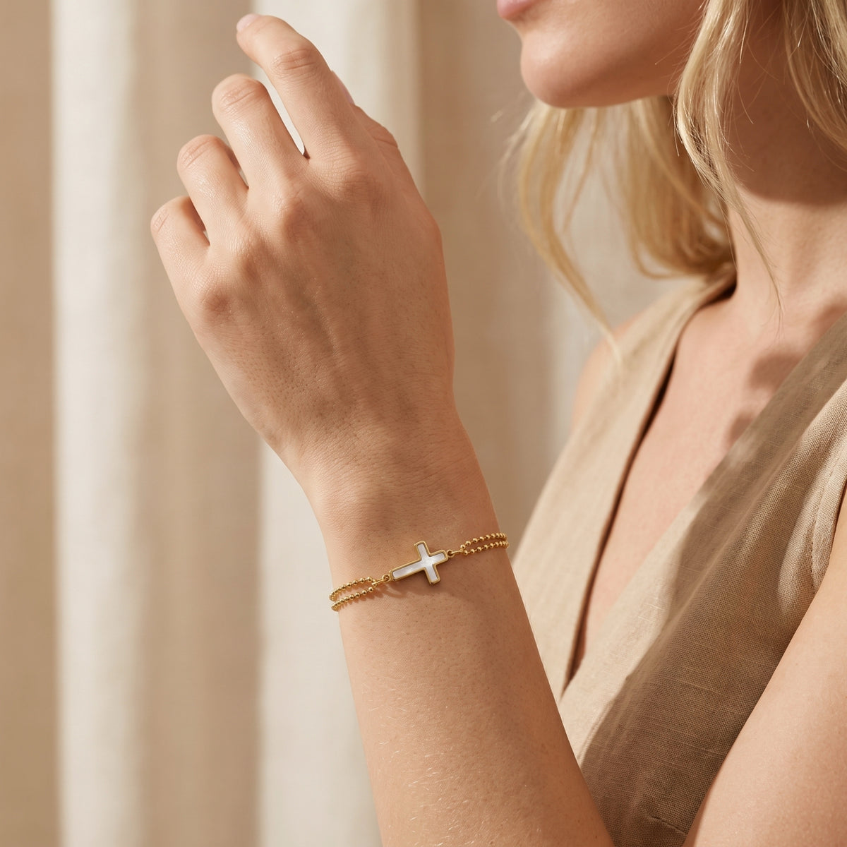 Close-up angled view of a model wearing the gold double-bead bracelet with a mother-of-pearl cross charm.