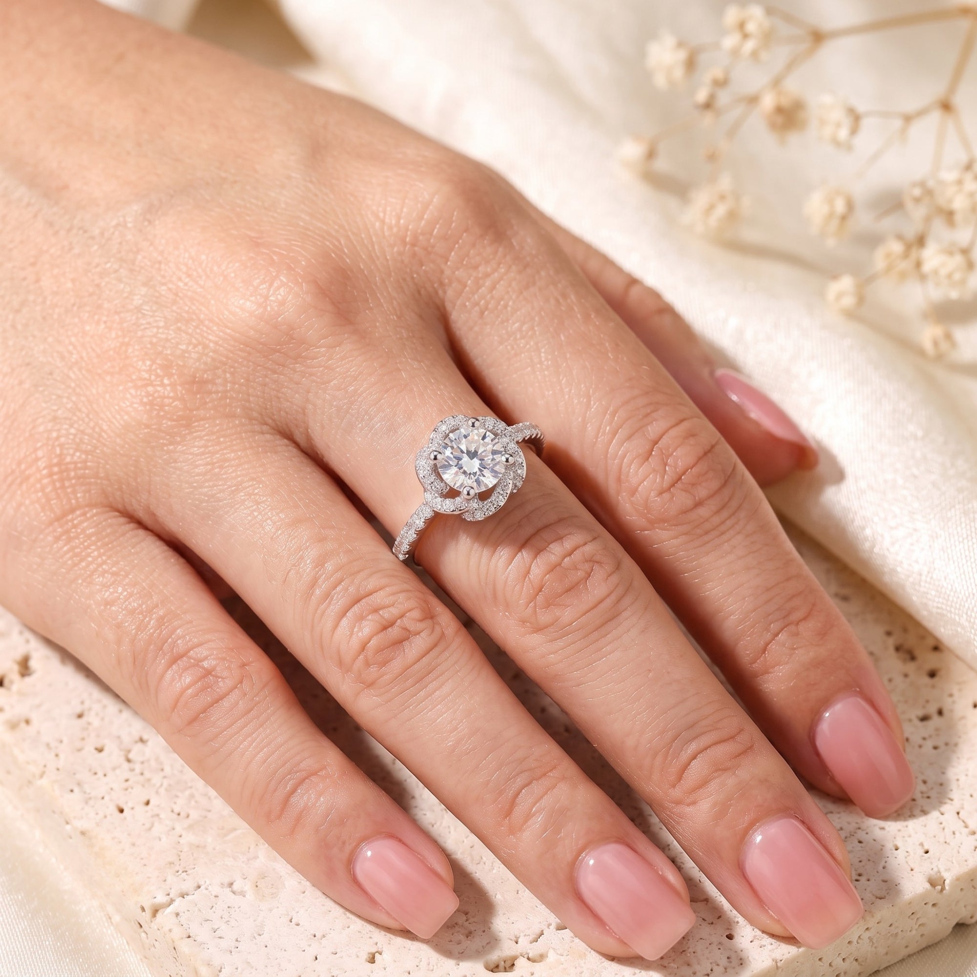 Top view of a sterling silver rosette swirl halo ring with a round simulated diamond on a model's hand.