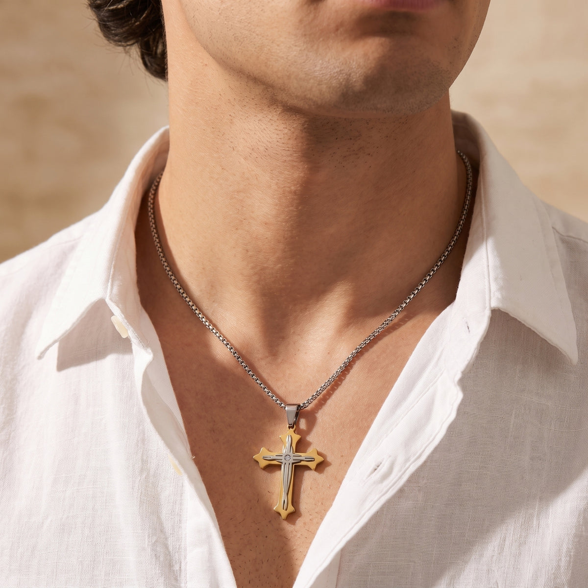 Frontal close-up of the two-tone cross necklace worn on a man's chest with an open white shirt.