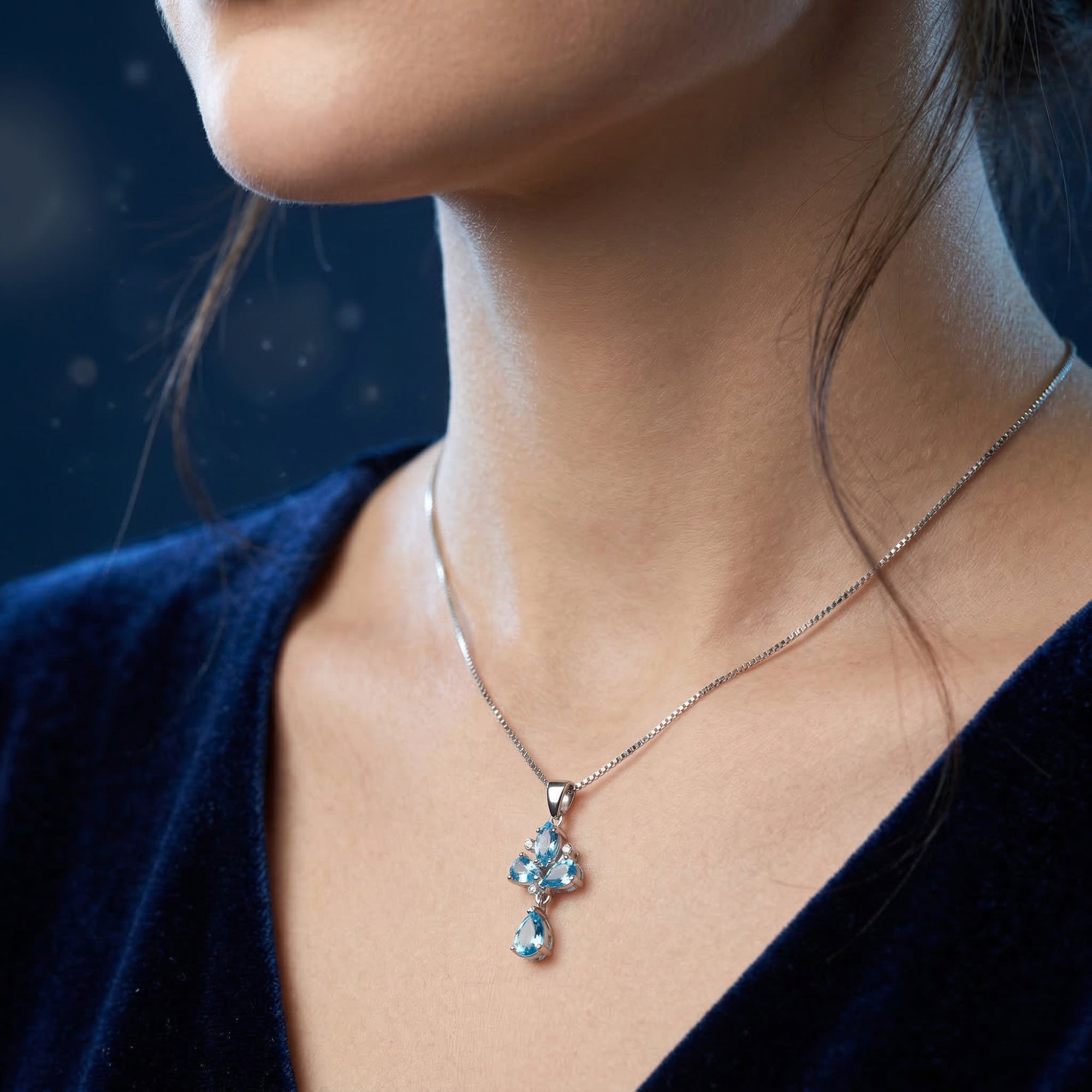 Silver Zephyrine necklace with blue topaz pendant worn by a model against a dark blue background.