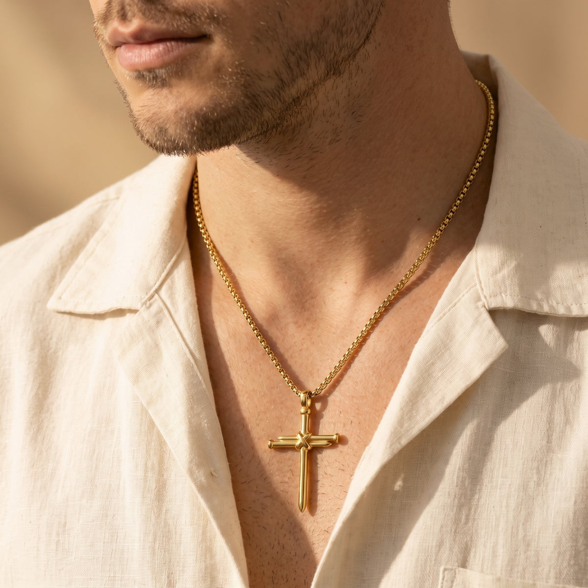 Man wearing the gold-tone bound nail cross necklace over an open cream shirt.