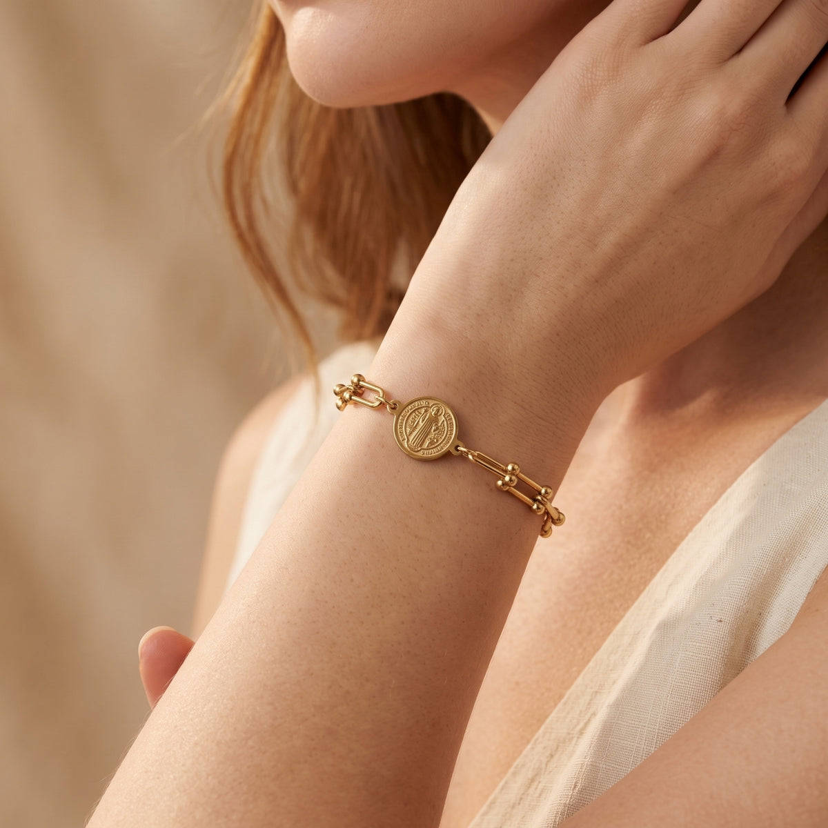 Close-up side view of a model wearing the gold-tone Saint Benedict medallion bracelet on her forearm.