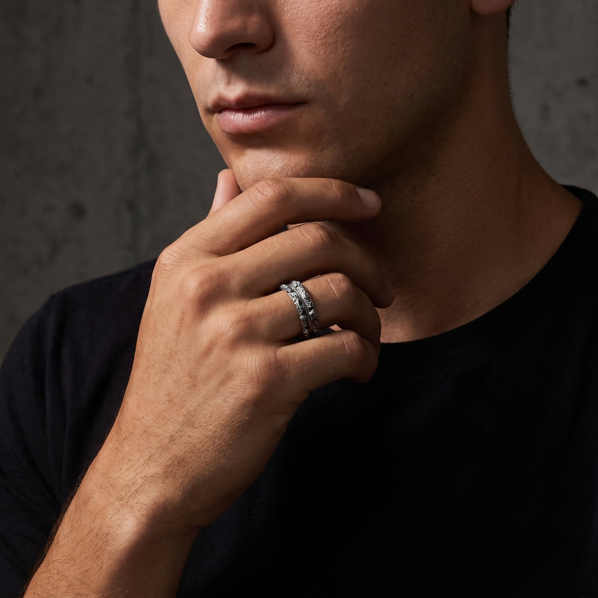 Close-up of a man wearing a textured silver ring with his hand resting against his chin.