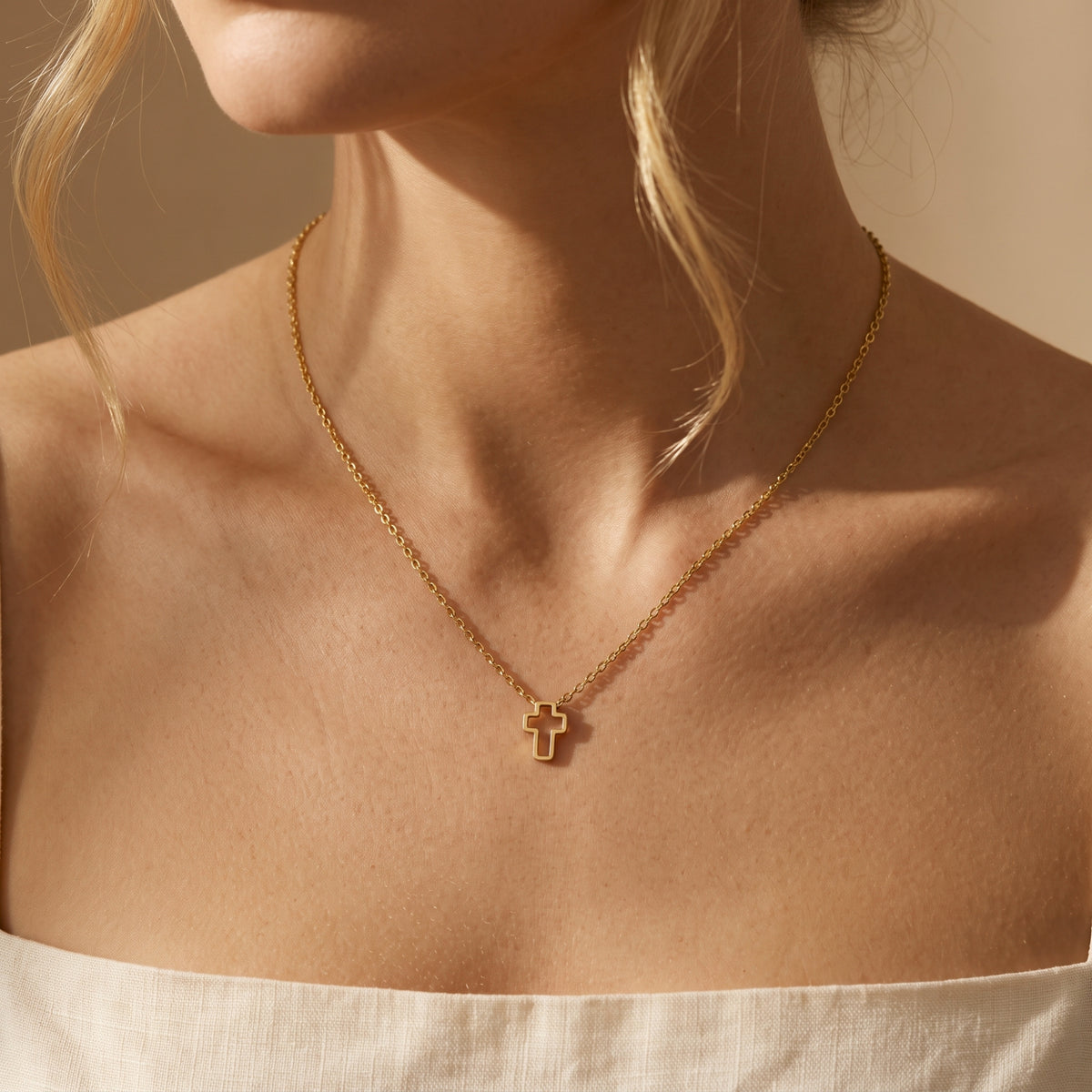 Model wearing a gold-tone openwork cross necklace above a white straight-neckline top.