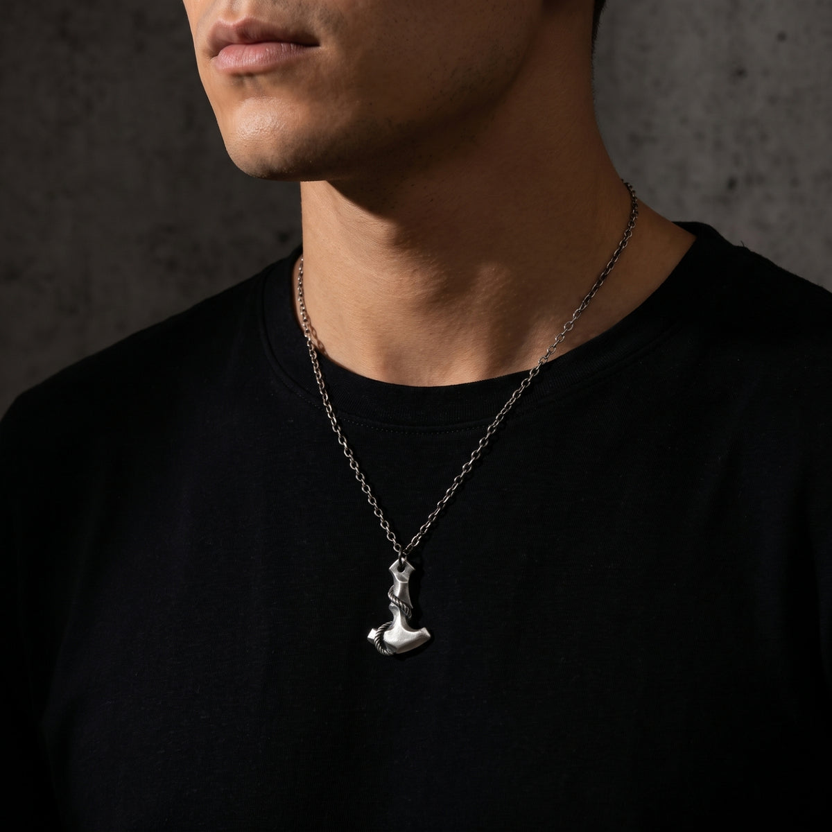 Torso view of a man wearing the silver Mjolnir pendant necklace with a black crewneck top.