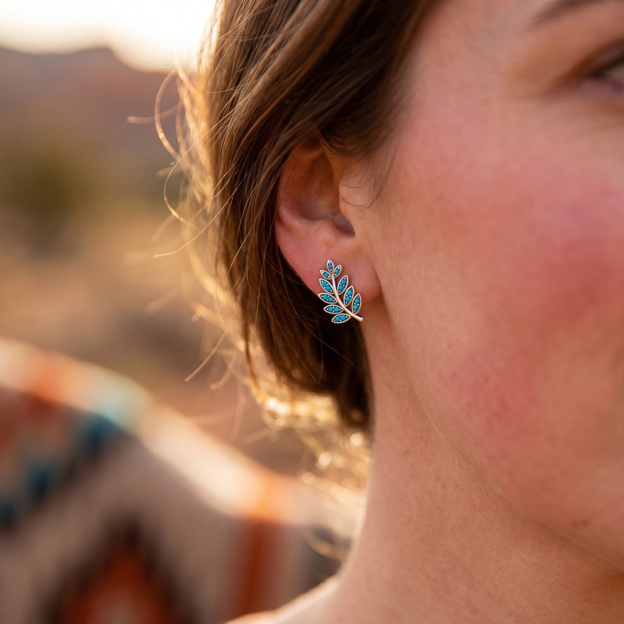 Profile view of a model wearing a silver Taos Turquoise earring with round stones in warm golden hour sunlight.