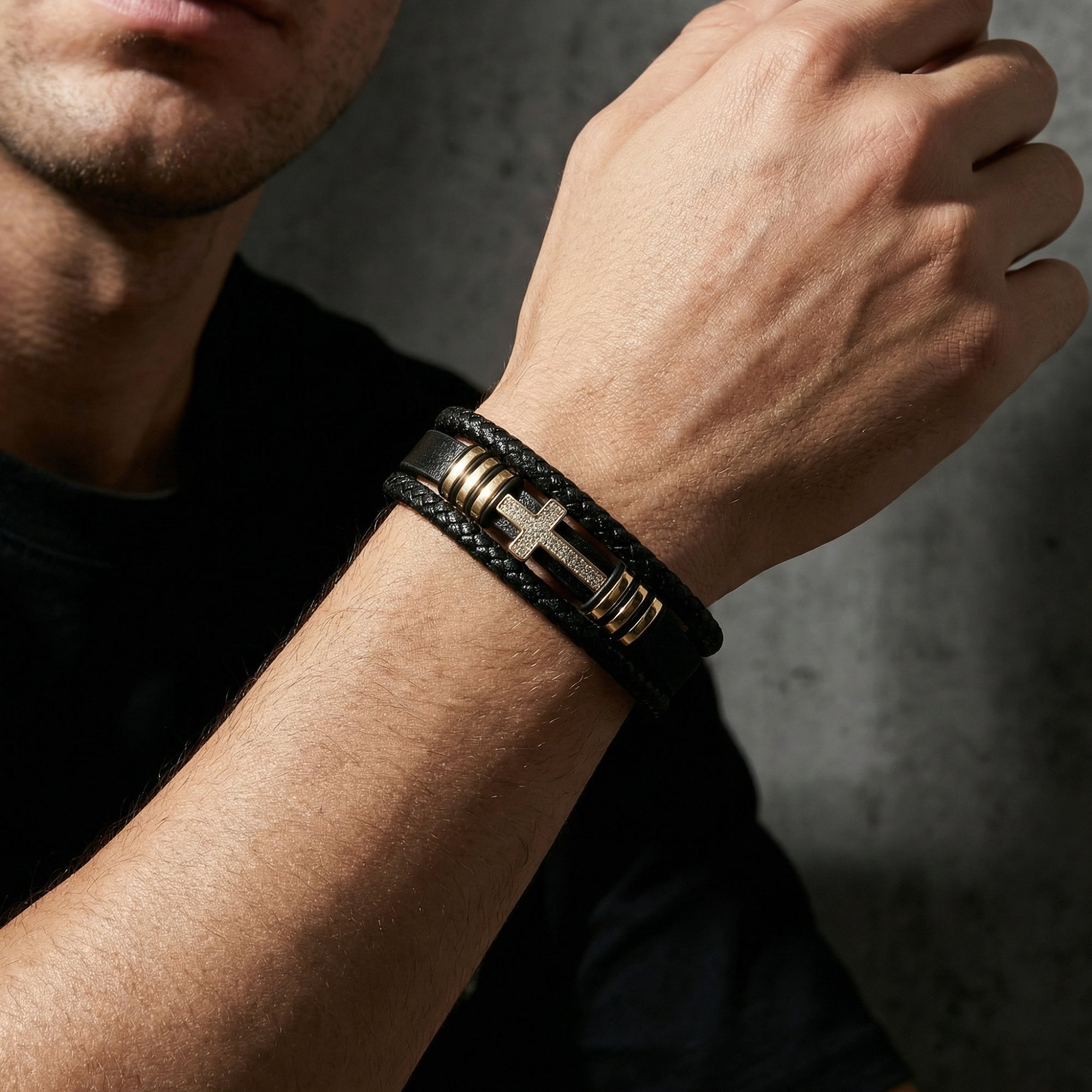 Gold-finished stainless steel cross bracelet with pavé stones on black braided leather, worn by a model.