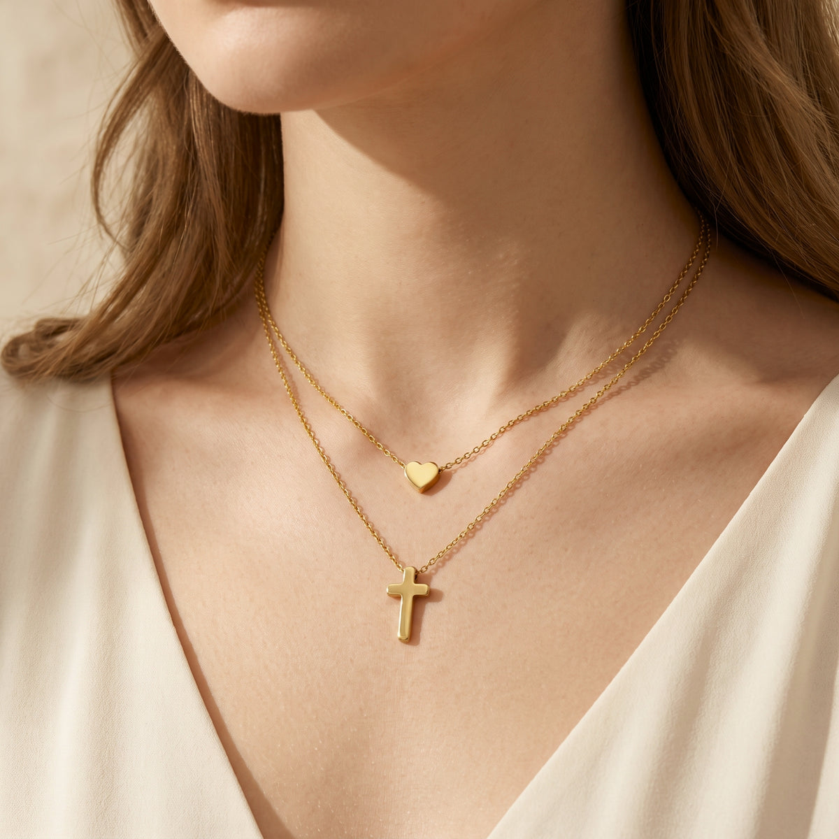 Front view of a woman wearing the layered gold-tone necklace with a small heart charm and cross pendant.