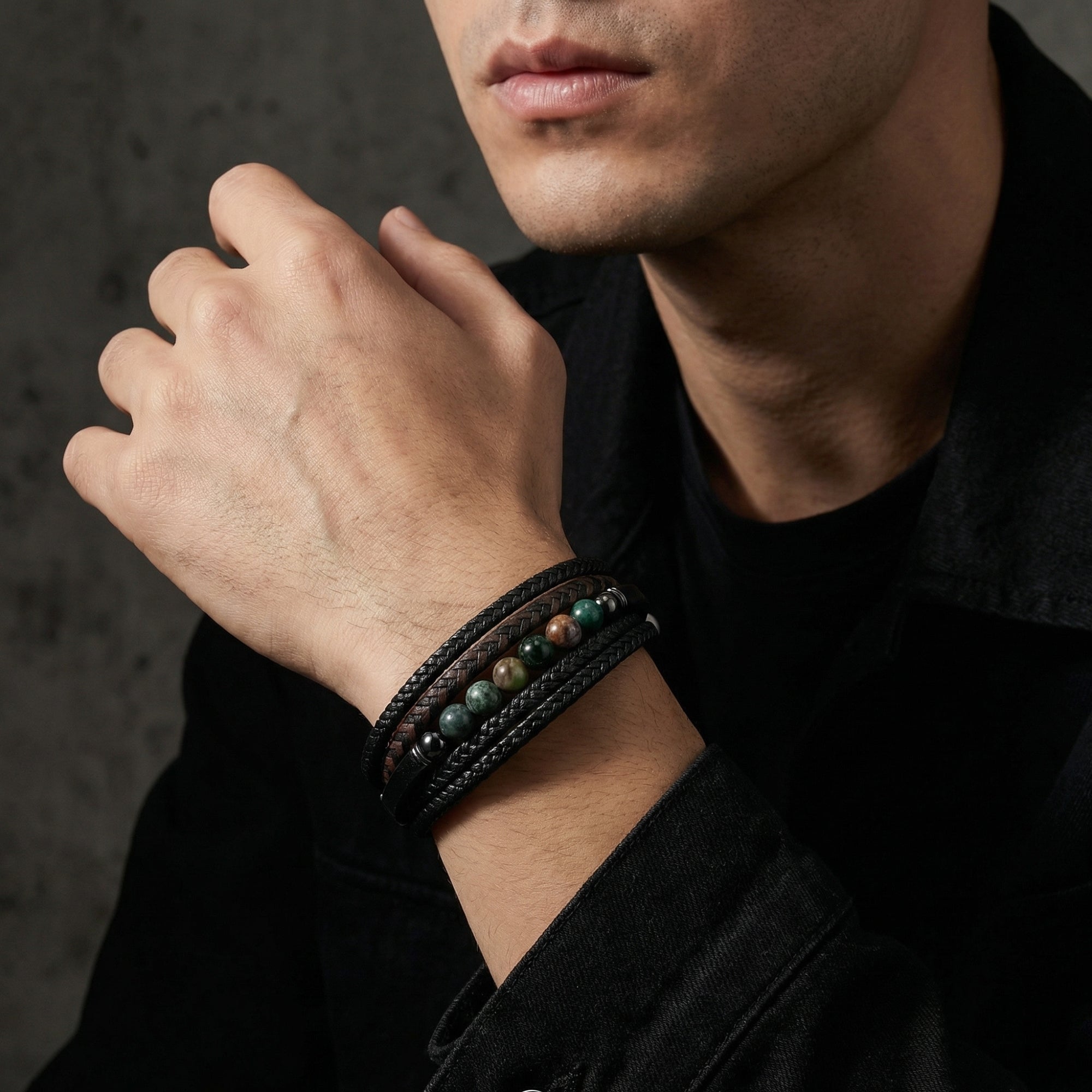 Close-up of a man wearing a multi-layer black leather bracelet with green and brown stone beads.