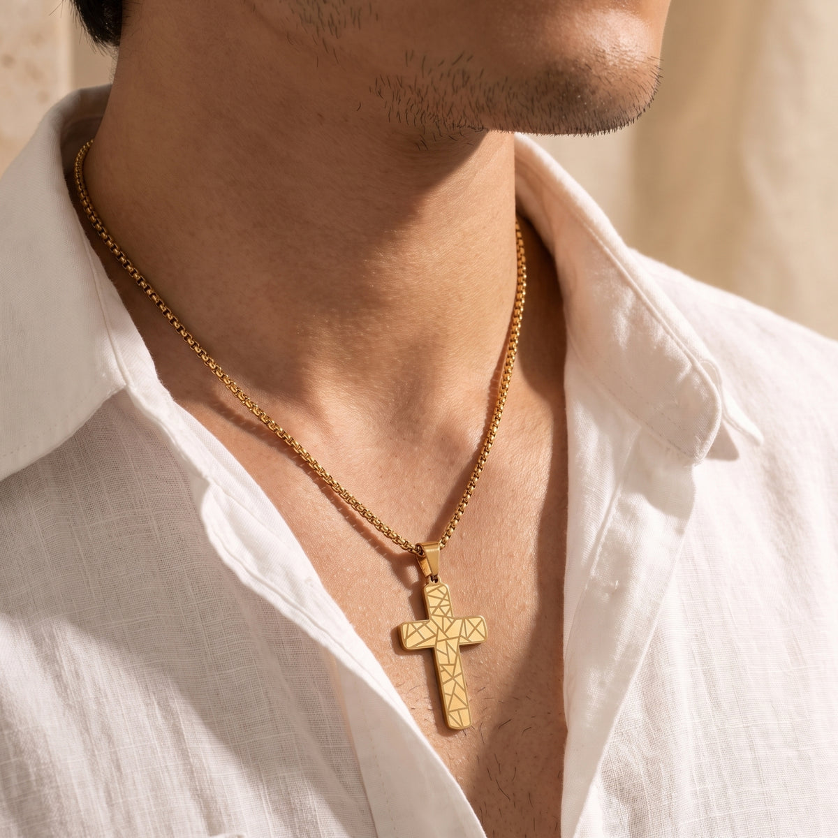 Close-up of a man wearing a gold-toned geometric cross pendant necklace against his chest in an open white shirt.