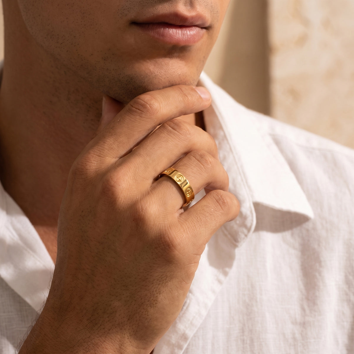 Close-up of a man resting his chin on his hand while wearing a gold-tone cross band ring.