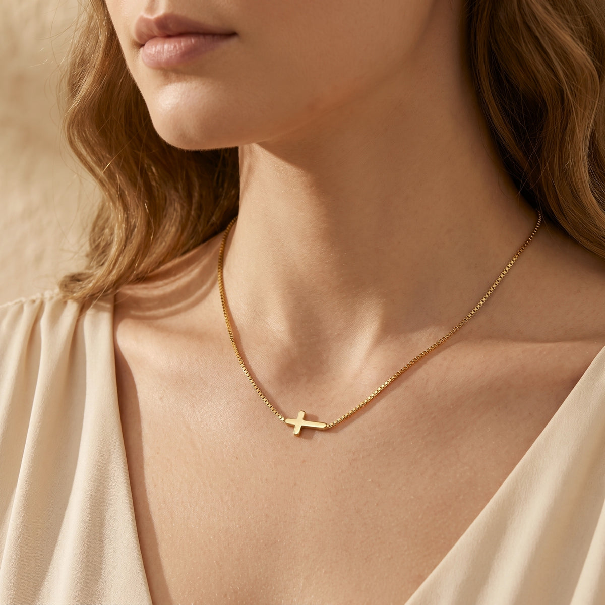 Close-up of a model wearing a gold-tone cross necklace with a cream draped garment.