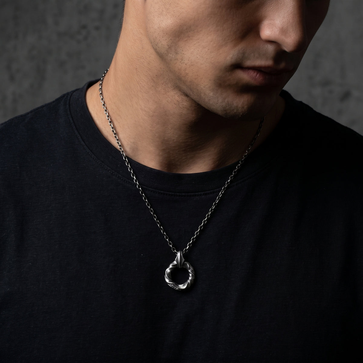 Close chest-up view of a model wearing the silver twisted circle pendant necklace while looking downward.