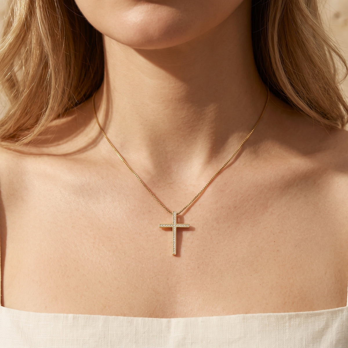 Front view of a model wearing a gold-tone pavé cross necklace over a cream strapless top.